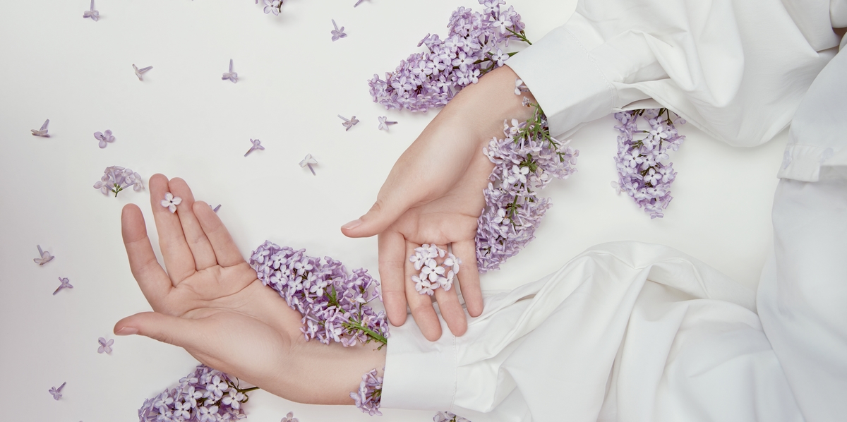 Natural woman cosmetics for hands made of lilac flowers and petals. Moisturize and soften the skin of the hands. Lilac flowers protrude from the sleeves of the arm